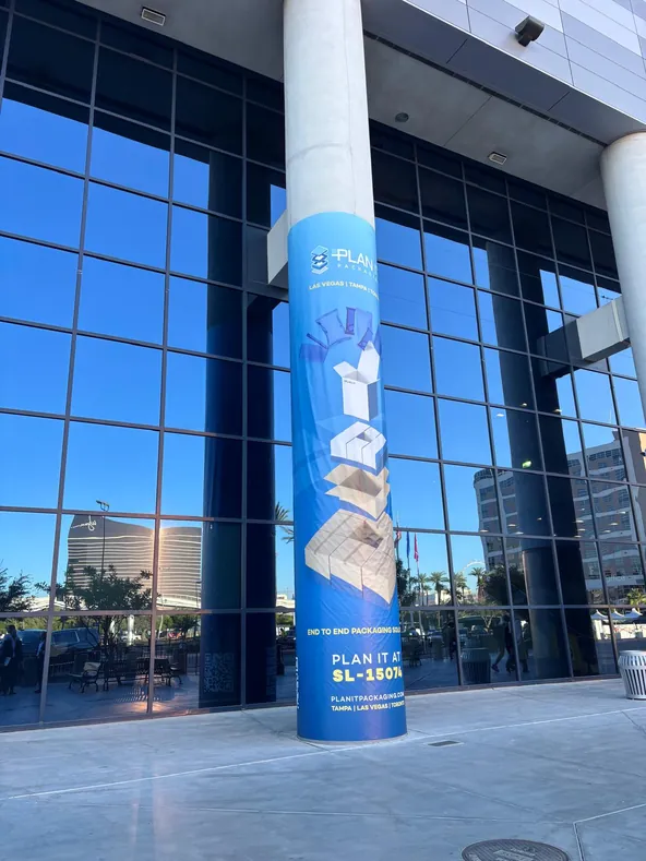 Tall printed trade show pillar outside a glass office tower